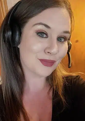 Close-up of a smiling woman wearing a black headset with a mic, indoors against a wooden background.