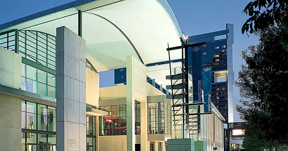 Modern glass-and-steel building with a curved roof and blue 'welcome' banners along the walkway exterior area.