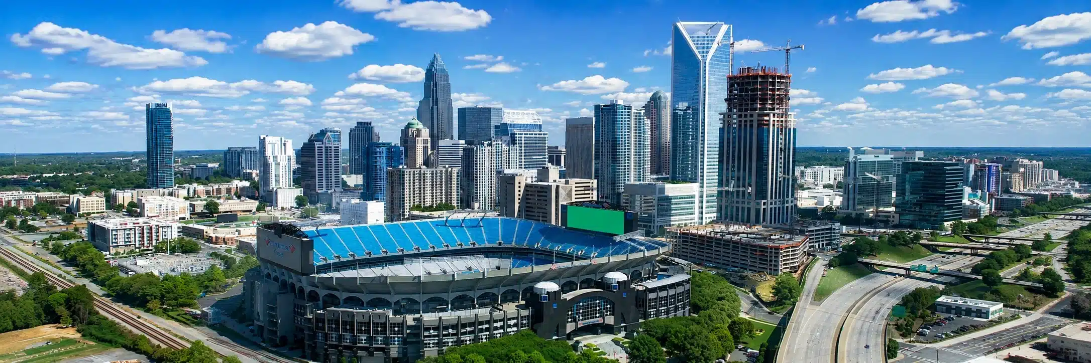 Aerial view of downtown Charlotte with tall skyscrapers and Bank of America Stadium in the foreground.
