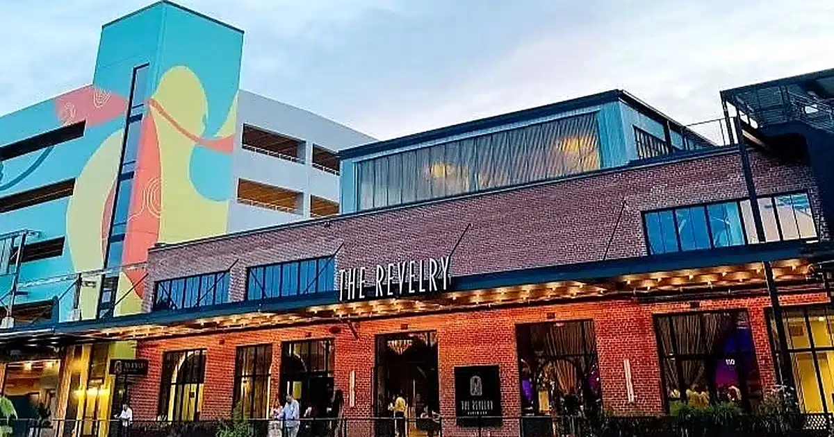 Brick storefront of The Revelry with string lights and a colorful mural on the adjacent building.