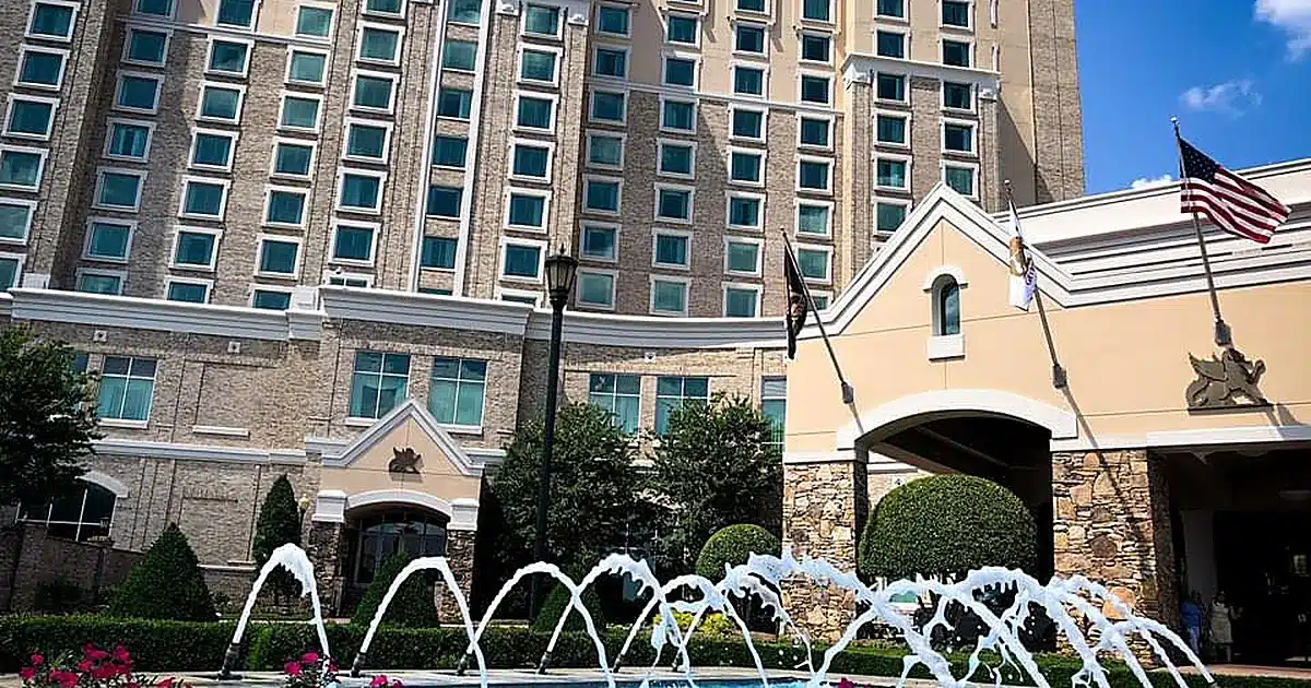 Hotel exterior with a multi-story beige brick facade, arched entrance, and a curved fountain in the foreground.