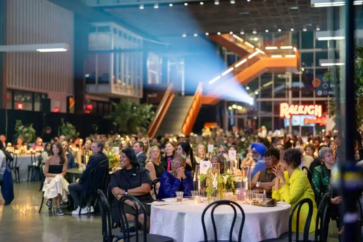 Guests seated at round tables during a formal banquet in a modern venue, with candles and a bright orange staircase in the background.
